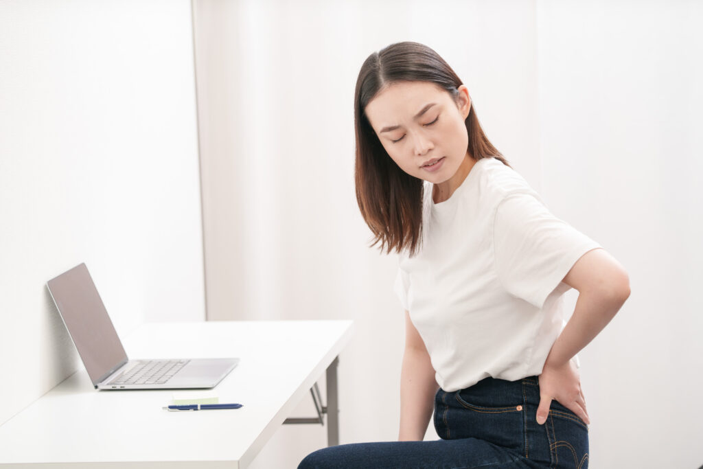 デスクワークの途中で腰を押さえる女性