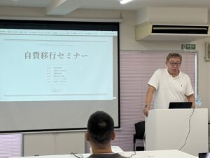 自費移行セミナーのスライドを前に講義する松村正隆理事