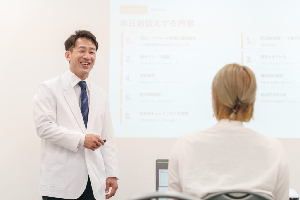 白衣の講師が勉強会でスライドを使って話している様子