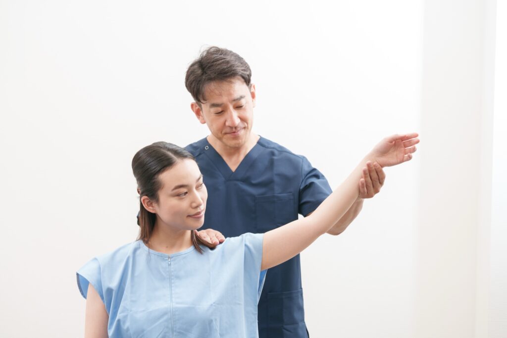 施術者が、座っている女性の腕を横に上げて、動く範囲を確かめている様子