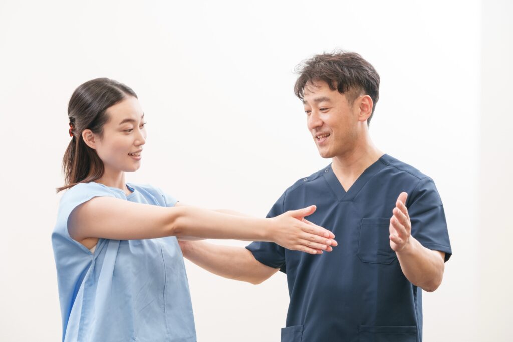 腕を前に伸ばした女性に、施術者が笑顔で体の状態を説明している様子