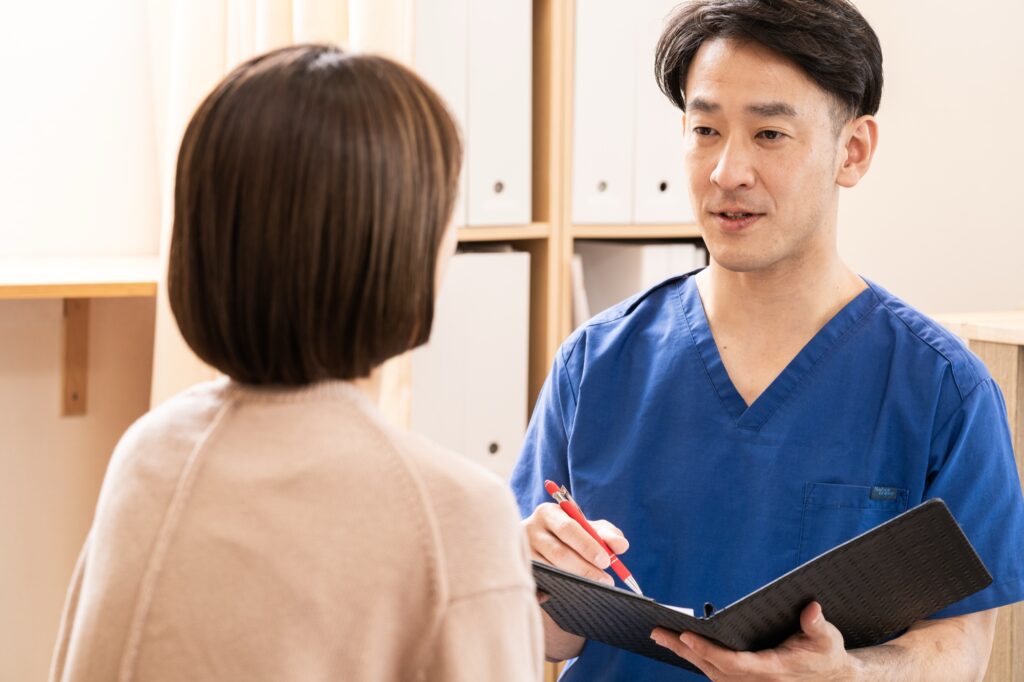 作尾大介が患者さんの話を聞きながら、カルテを手に語りかけている様子