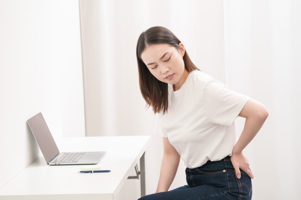 机の前で、腰に手を当ててつらそうにしている女性