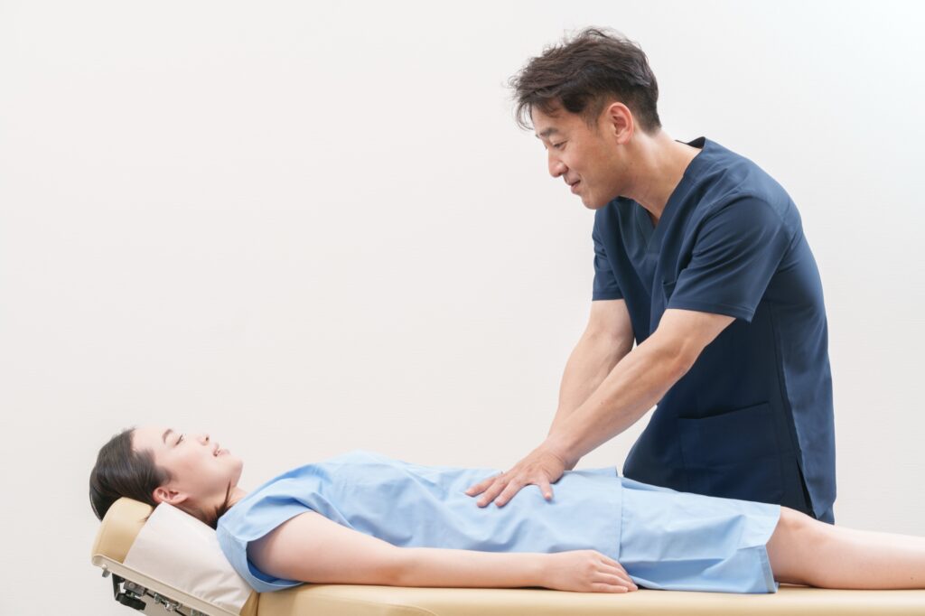 あお向けに寝た女性のお腹のあたりに、施術者が手を当てて触診している様子