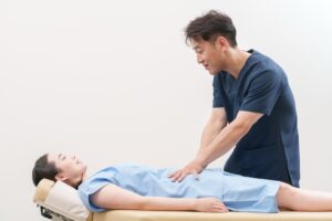あお向けに寝た女性のお腹のあたりに、施術者が手を当てて触診している様子