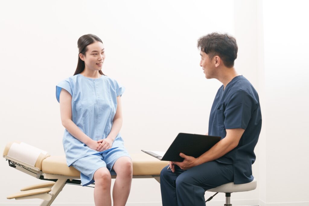 施術ベッドに座る女性に、施術者がバインダーを持って初めての問診をしている様子