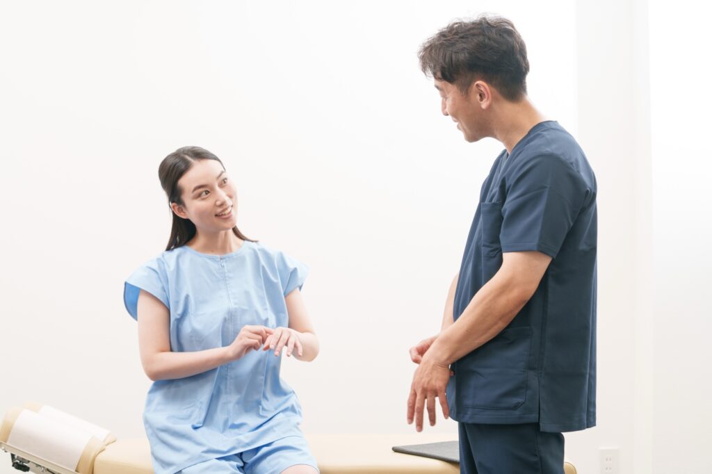 施術ベッドに座る女性の話を、施術者が立ったまま耳を傾けて聞いている様子