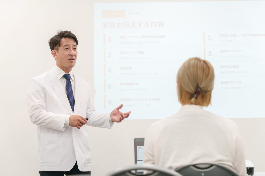 勉強会で、白衣の講師がスライドを使って受講者に話している様子